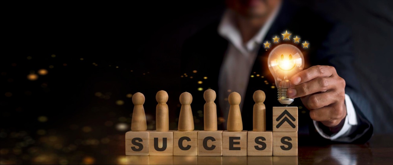 Figurines en bois sur des cubes formant le mot « Success », une ampoule allumée surmontée d'étoiles