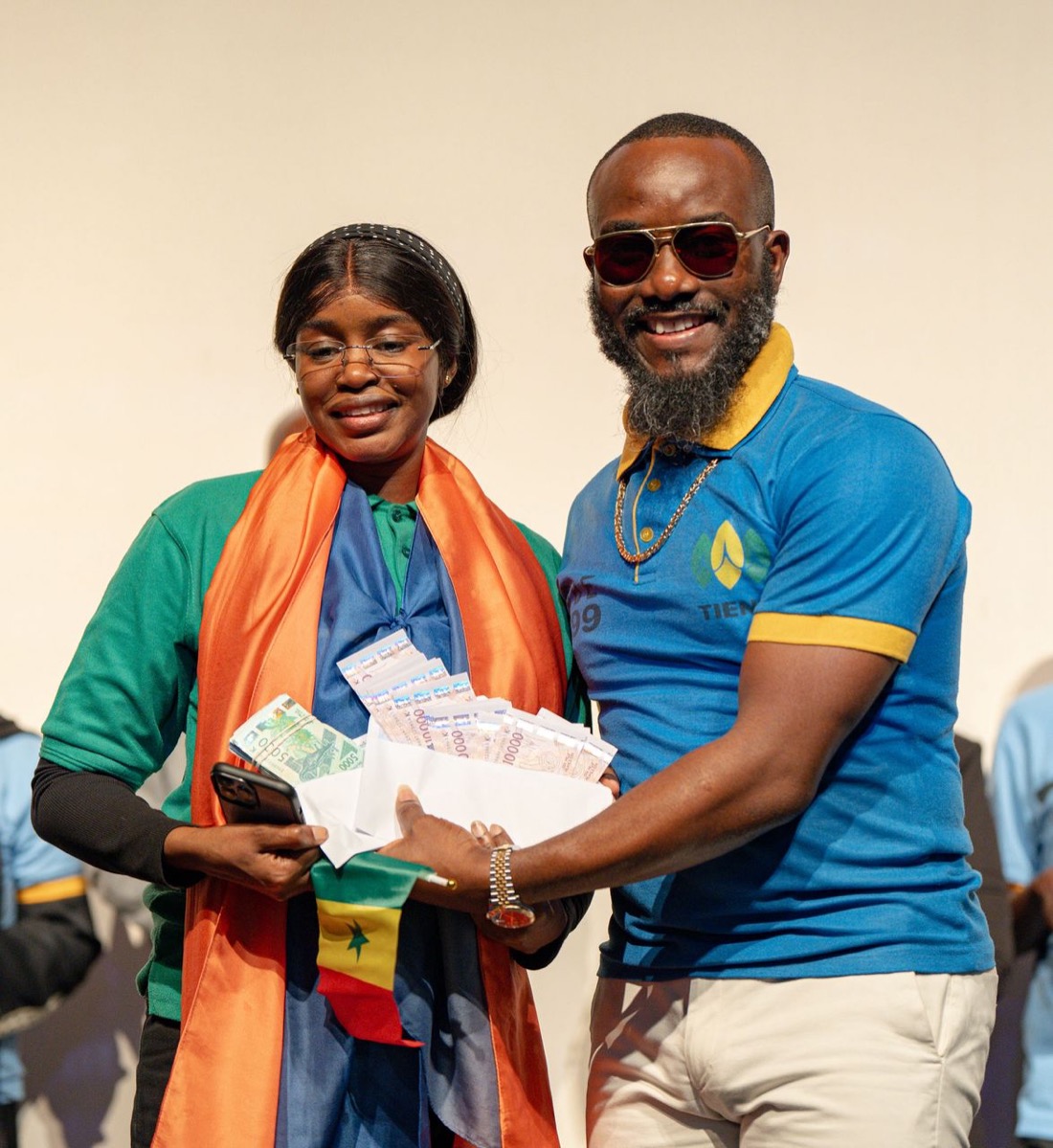 Deux membres TIENS DS-COM présentant fièrement une récompense, drapeau du Sénégal sur les épaules